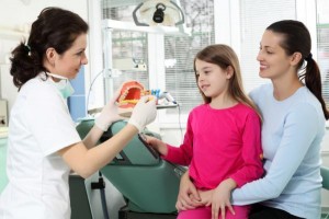 Female dentist demonstrating toothbrushing to a young girl and her mom